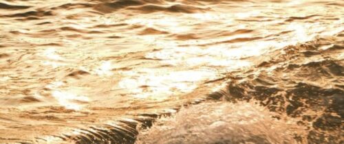 Experience the serene beauty of ocean waves illuminated by the golden hues of sunset.