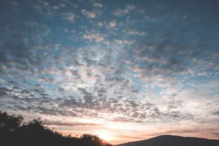 Silhouettes of hill and woodland under bright sky with fluffy clouds at sunset