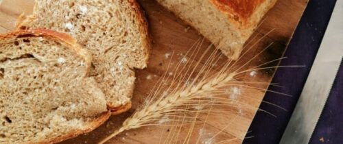 Sliced whole wheat bread on a wooden board with wheat stalks and a knife, perfect for baking and food photography.