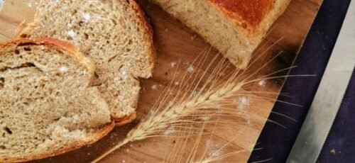 Sliced whole wheat bread on a wooden board with wheat stalks and a knife, perfect for baking and food photography.