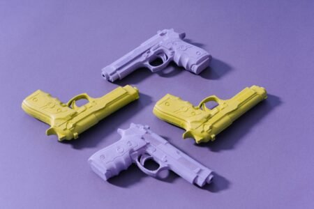 Four toy guns in pastel hues on a purple surface, artistic minimalism.