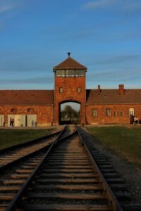 View of the iconic Auschwitz-Birkenau entrance gate at sunset in Oświęcim, Poland.