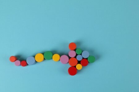 A vibrant arrow composed of colorful cylinders against a minimalist blue backdrop.