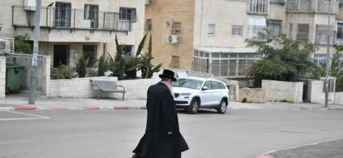 a man walking across a street next to a white car