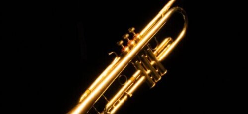 A shiny golden trumpet beautifully highlighted against a deep black background.
